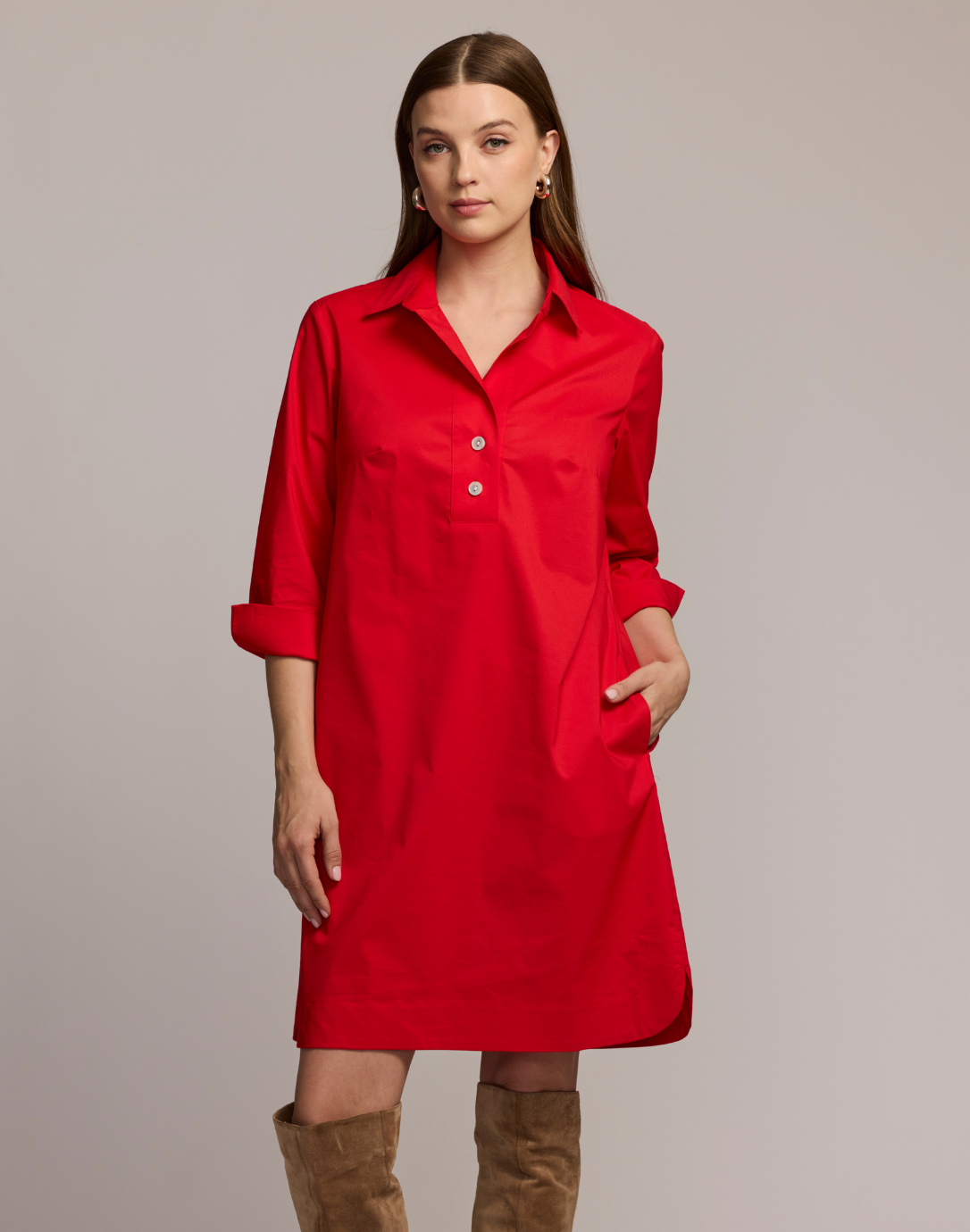 Woman wearing a red dress with brown boots on a plain background