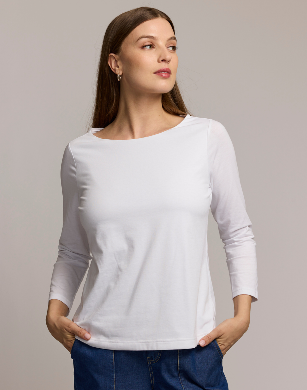 Woman wearing a white long-sleeve boat neck top against a plain background