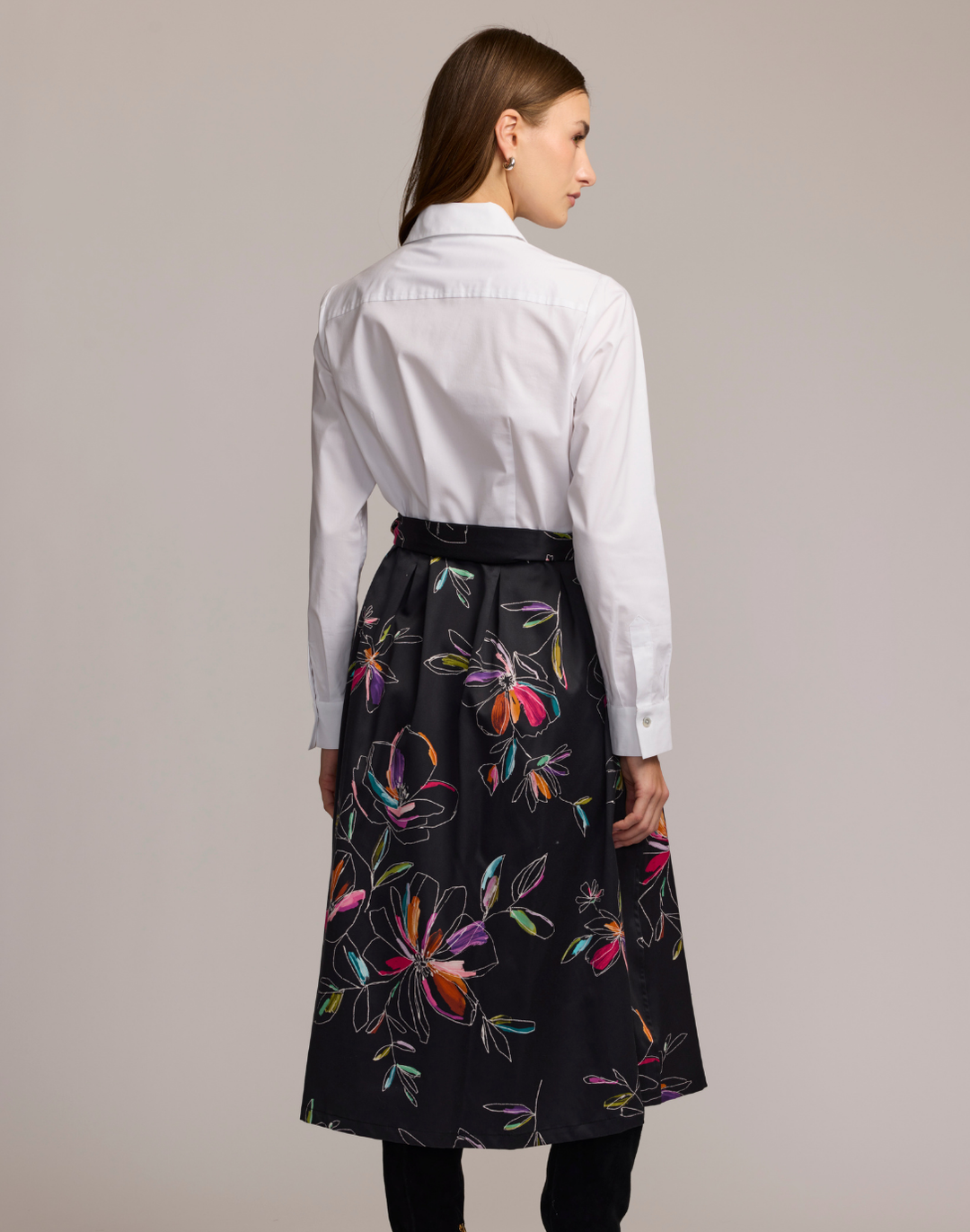 Woman wearing a shirt dress with a white floral embroidered top and black floral patterned skirt against a plain background. 