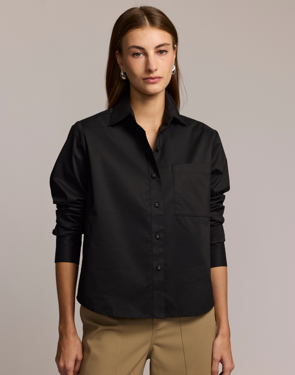 Woman wearing a black shirt and beige pants against a neutral background