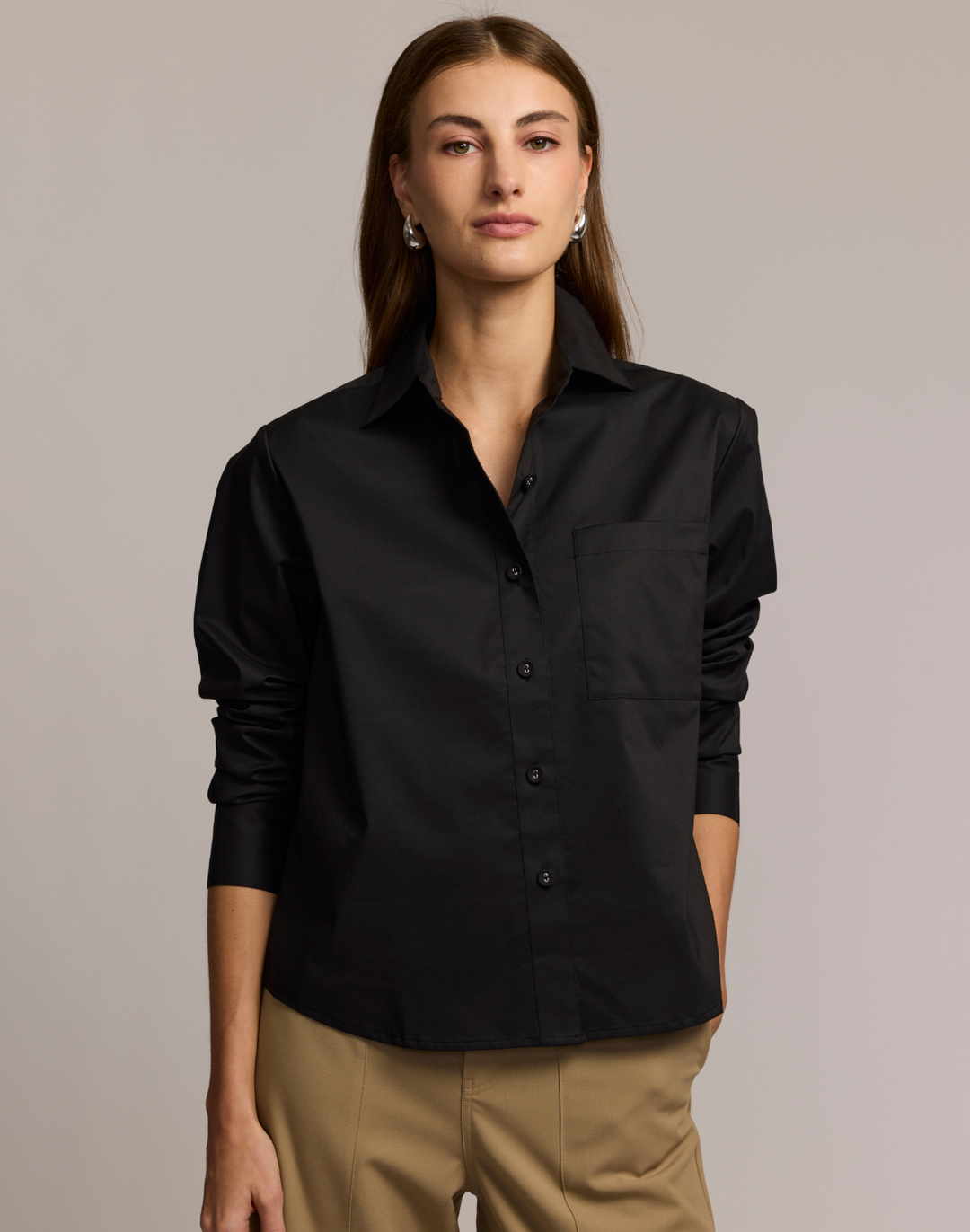 Woman wearing a black shirt and beige pants against a plain background