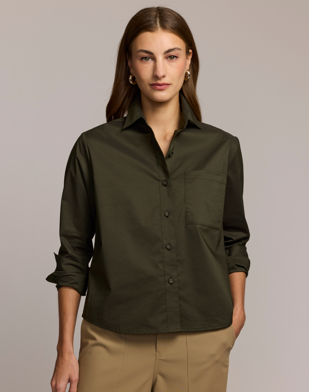 Woman wearing a dark green shirt with rolled-up sleeves against a neutral background