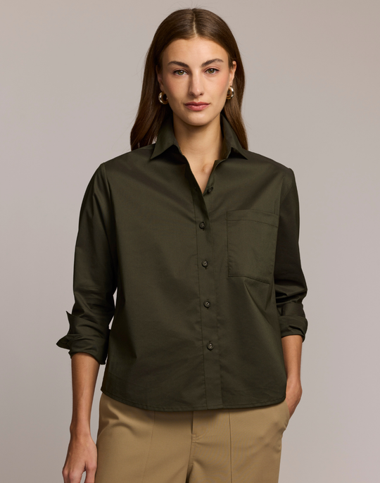 Woman wearing a dark green shirt with rolled-up sleeves against a neutral background