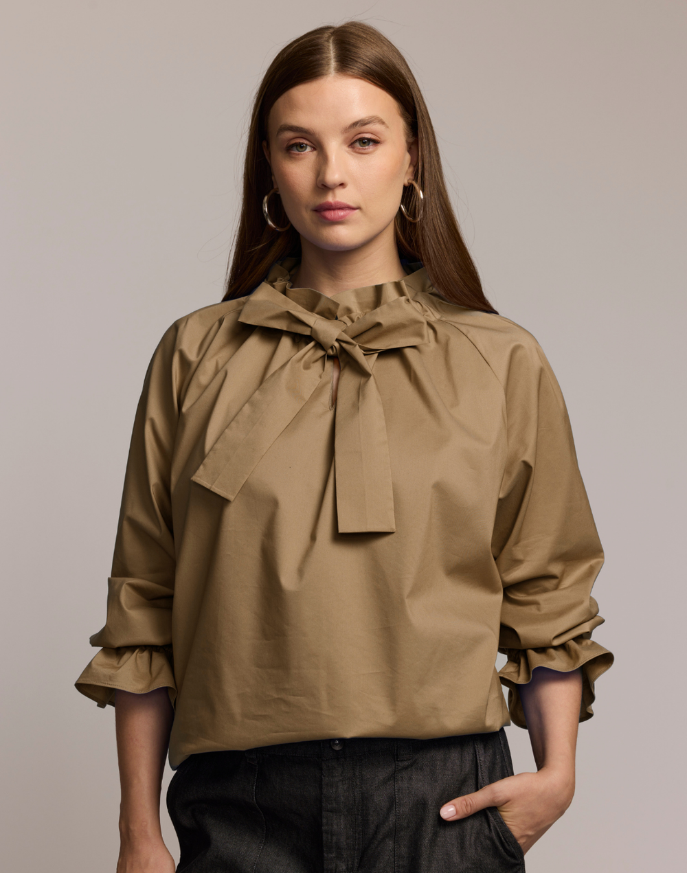Woman wearing a beige blouse with a large bow neck detail against a plain background