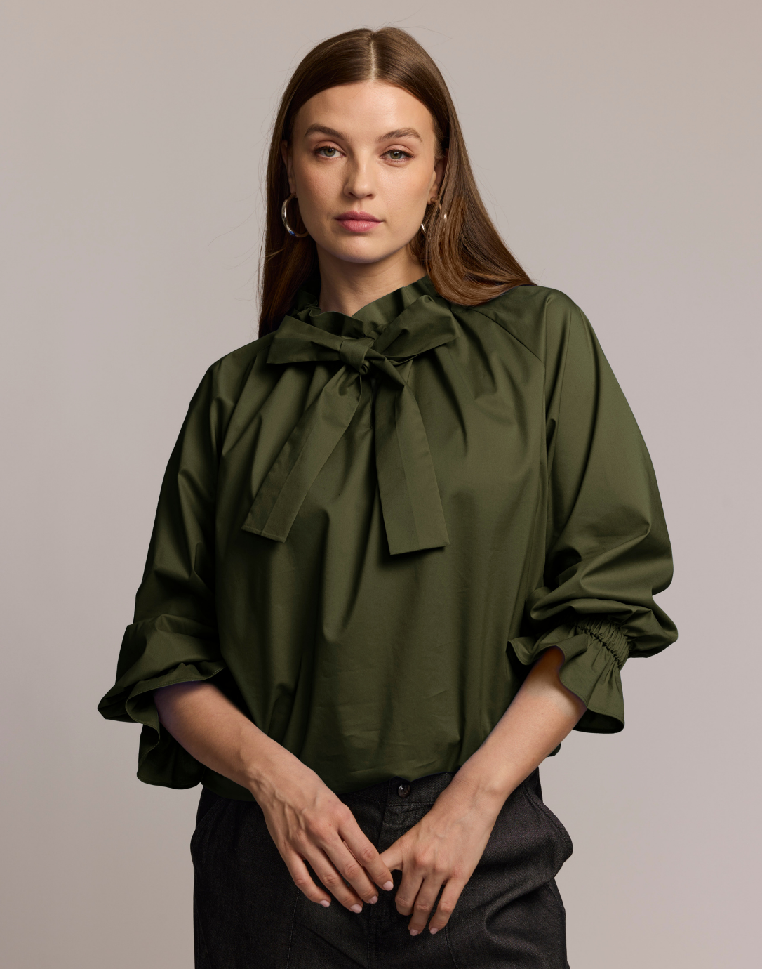 Woman wearing a green blouse with a bow neck detail on a plain background