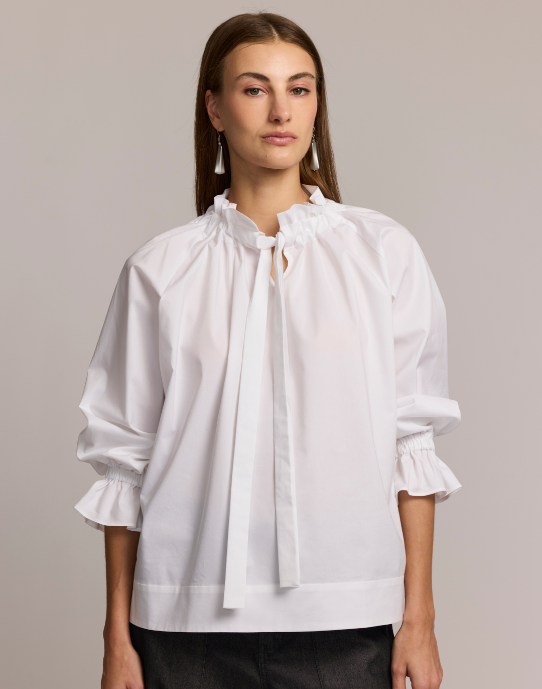 Woman wearing a white blouse with tie neck and ruffled sleeves against a plain background