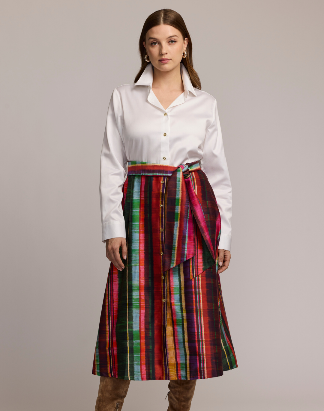 Woman wearing a shirtdress with  a white top and colorful striped skirt on a plain background