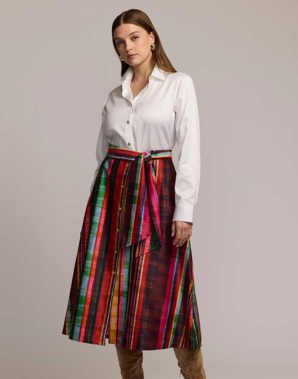 Woman wearing a shirtdress with  a white top and colorful striped skirt on a plain background