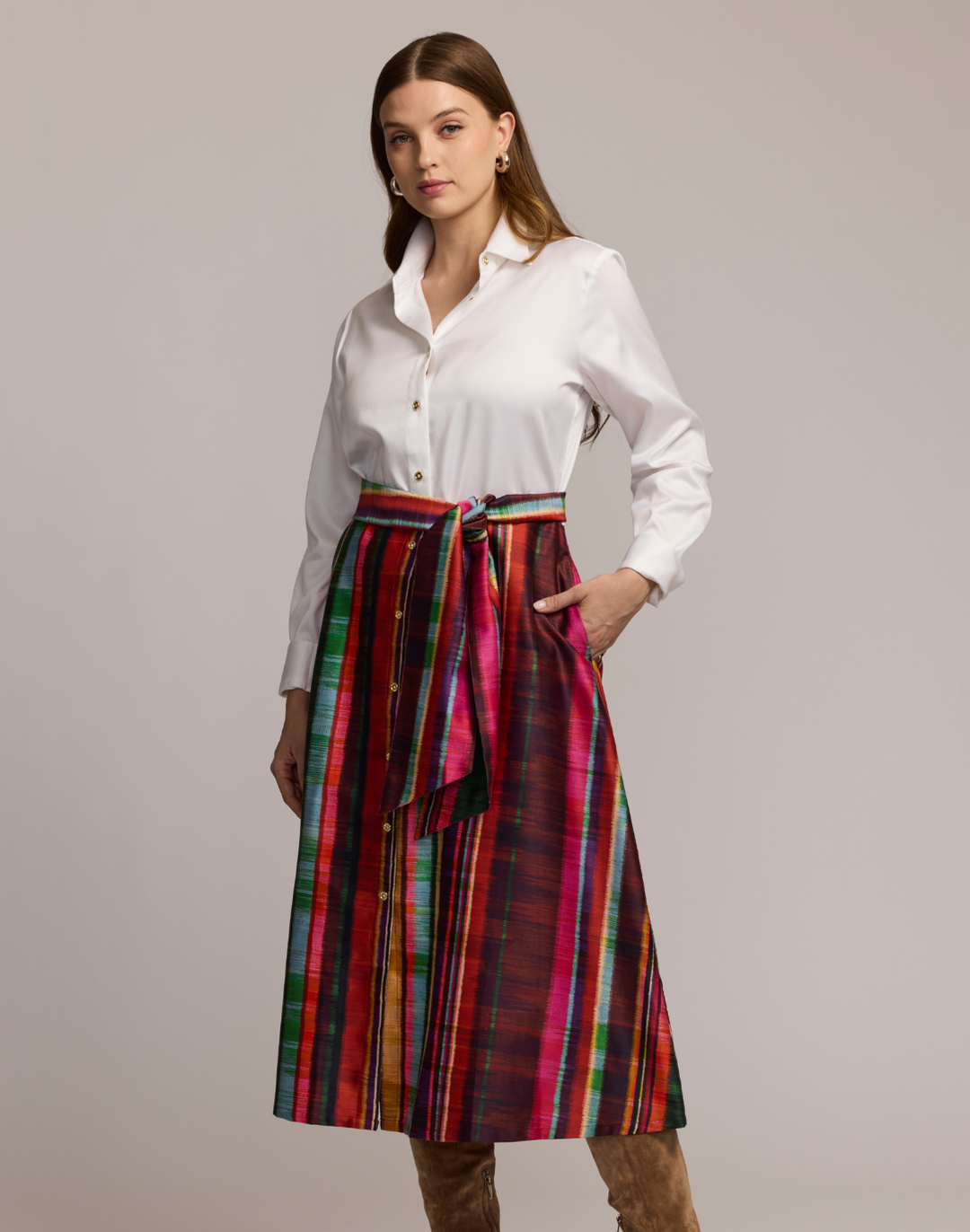 Woman wearing a shirtdress with  a white top and colorful striped skirt on a plain background