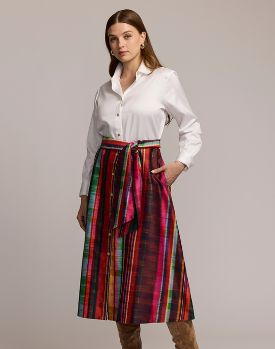 Woman wearing a shirtdress with  a white top and colorful striped skirt on a plain background
