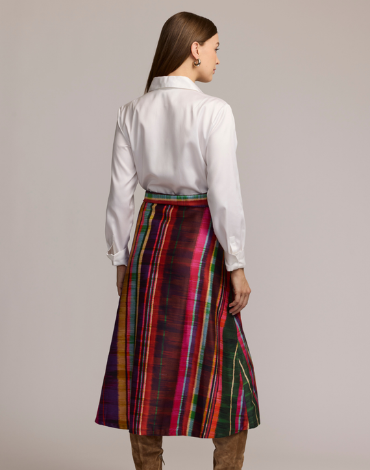 Woman wearing a shirtdress with  a white top and colorful striped skirt on a plain background