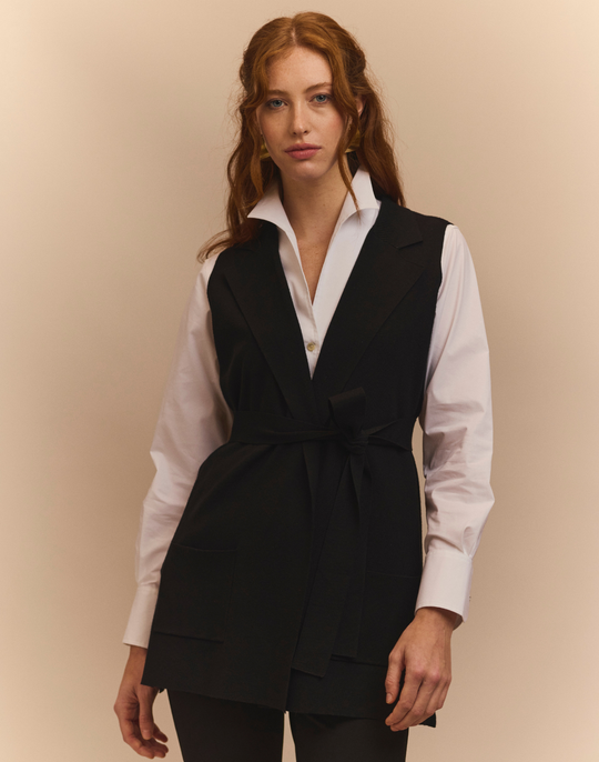 Woman wearing a black vest over a white shirt against a beige background