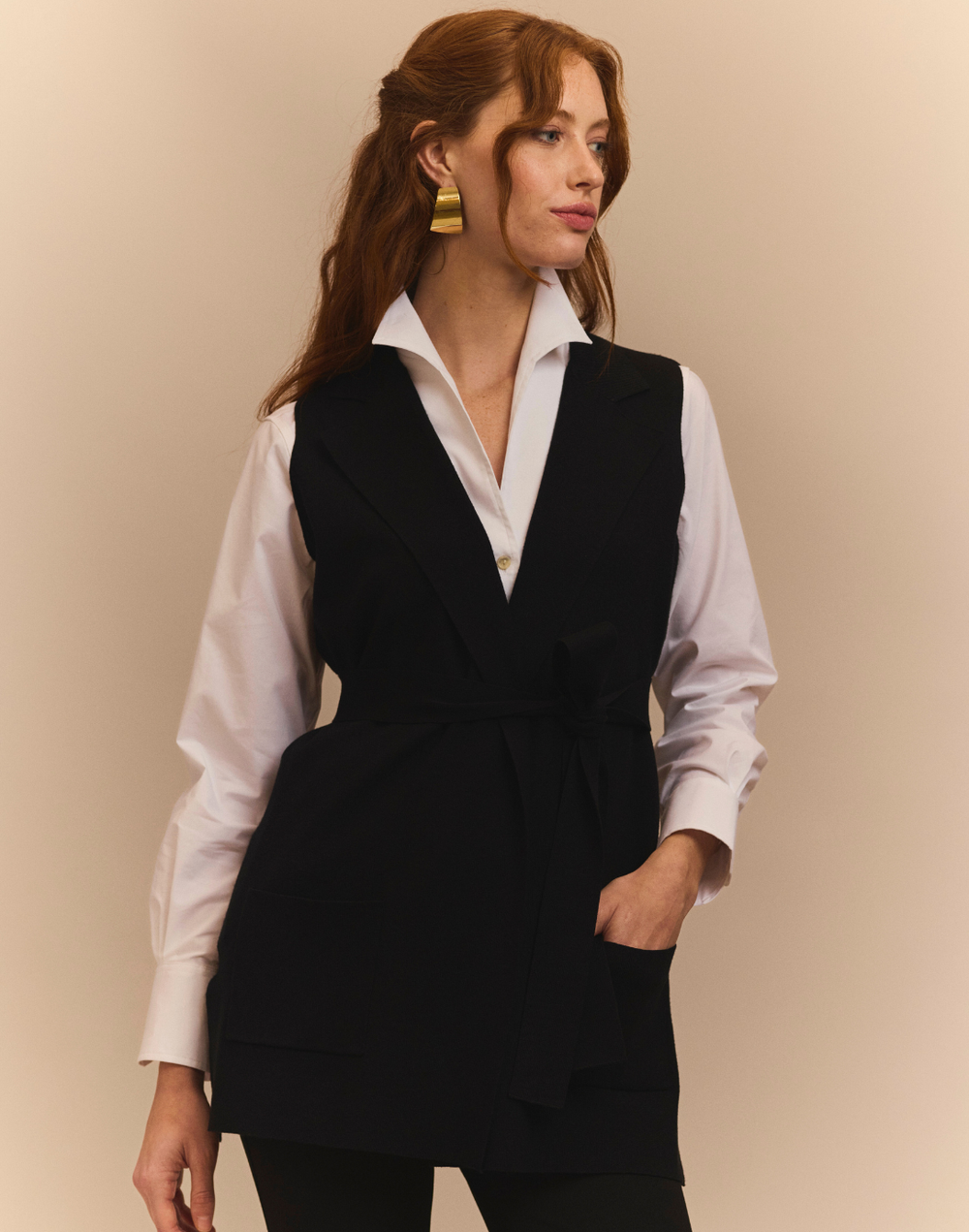 Woman wearing a black vest over a white shirt against a beige background