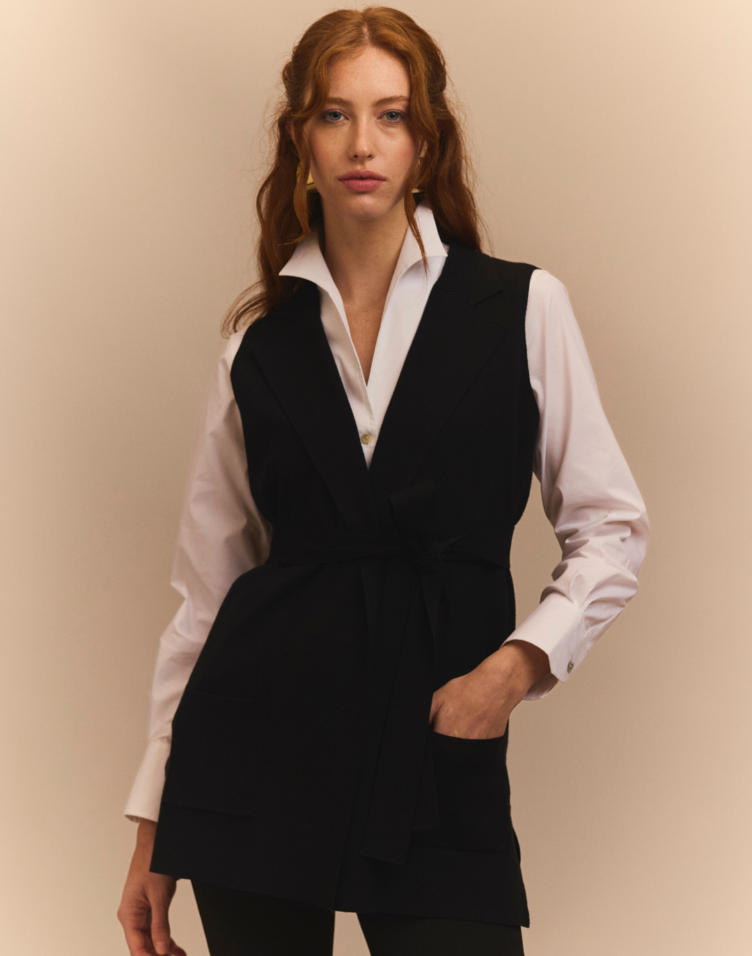 Woman wearing a black vest over a white shirt on a beige background