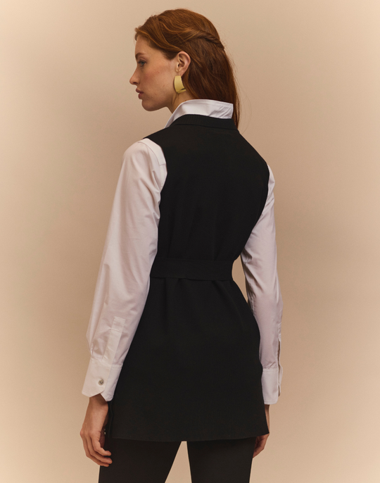 Woman wearing a black vest over a white shirt on a beige background